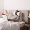 Man comfortably working on his laptop in bed enjoying the technology of the anti snoring pillow | The Snorinator